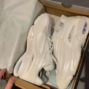 Vita chunky sneakers från Nike - Säljer ett par riktigt feta vita sneakers från Nike med chunky sula och futuristisk design. Skorna har snörning och detaljer i syntetmaterial som ger en clean och modern vibe. Perfekta för dig som vill sticka ut med din stil.