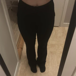 Svarta bootcut byxor med hög midja - Säljer ett par svarta byxor med bootcut-snitt och hög midja. Byxorna har en klassisk, stilren look och sitter snyggt över höften. Passar dig som gillar en tidlös och clean stil. Materialet känns mjukt och följsamt mot kroppen.