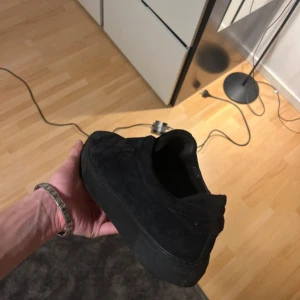 Axel arigatos  - Säljer ett par svarta Axel arigatos med platt sula och tjock plattform. Skorna är gjorda i mocka och har en stilren, minimalistisk look utan snörning. Perfekt för dig som gillar enkel och clean stil. Passar till jeans eller andra casual outfits. Lite söndriga där framme men kan fixas enkelt med lim annars bra skick