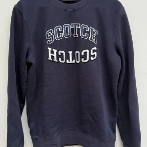 Mörkblå Scotch & Soda sweatshirt - Mörkblå sweatshirt från Scotch & Soda med broderad text 'SCOTCH' i vitt och blått på bröstet. Tröjan har rund hals, långa ärmar och mjukt material i bomull. Perfekt för chill dagar och snygg till jeans eller joggers.