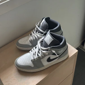 Nike Air Jordan 1 Mid grå/vit - Säljer ett par Nike Air Jordan 1 Mid i grått och vitt    Storlek 41 men borde även passa till den med storlek 42