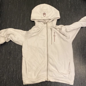 Vit hoodie från Sail Racing - Vit hoodie från Sail Racing med dragkedja framtill och en extra bröstficka med dragkedja. Tröjan har huva med broderad logga och långa ärmar. Perfekt för dig som gillar vill ha en men inte vill betala fullt pris!
