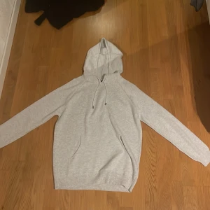 Ljusgrå hoodie från Felix Hardy - Snygg ljusgrå hoodie från Felix Hardy med huva och snörning. Tröjan har långa ärmar, ribbade muddar och en klassisk känguruficka framtill. Perfekt för chill dagar och enkel att matcha med jeans eller joggers.