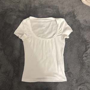 Vit ribbad kortärmad topp - Säljer en vit ribbad topp med korta ärmar och rundad, djup halsringning. Materialet är mjukt och stretchigt, perfekt för en chill och clean look. Passformen är slim och toppen är enkel att matcha med jeans eller kjol.