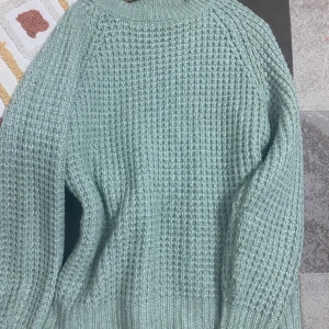 Ljusgrön stickad tröja från 157 - Mysig ljusgrön stickad tröja från 157 i storlek S. Tröjan har ett grovt, ribbat mönster och rund halsringning. Perfekt för dig som gillar chill och comfy vibes under höst och vinter. Snygg att styla med jeans eller mjukisbyxor.