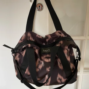 Mönstrad axelväska från DAY ET - Cool axelväska från DAY ET med svart och brun mönstrad design. Väskan har breda svarta axelband, dragkedja upptill och ett stort huvudfack med innerficka. Perfekt för dig som vill ha en rymlig och snygg väska till vardagen.