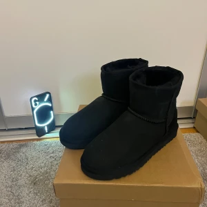Svarta UGG boots i mocka - Sprillans nya Uggs! Svarta UGG boots i klassisk modell med rund tå och platt sula. Tillverkade i mjuk mocka med fårskinnsfoder för extra värme. Diskret UGG-logga bak på hälen. Perfekta för kalla dagar och riktigt sköna att ha på sig.