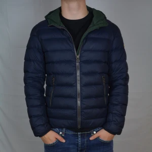 Colmar Jacka - Riktigt fet marinblå dunjacka med grön insida från Colmar. Jackan är i bra skick men har en liten lagning på bröstet. Jackan är i storlek M, men passar även S.                                                          Vid frågor eller funderingar är det bara att höra av sig, och kom ihåg, alltid 14 dagars ångerrätt hos oss på Revalo!