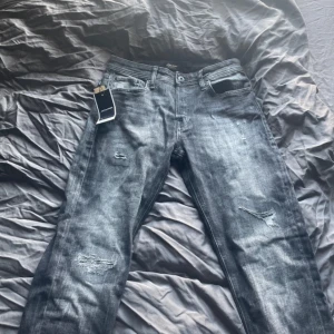 Jack & Jones mörkgrå tapered jeans - Snygga mörkgrå jeans från Jack & Jones med tapered passform. Jeansen har slitna detaljer. Materialet är jeans med en tvättad look och coola slitningar på benen. Pris kan alltid diskuteras, skriv vid funderingar!