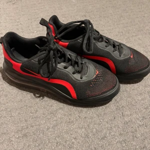 Svarta och röda Nike sneakers - Säljer ett par svarta och röda Nike sneakers med snygg design och sportig känsla. Skorna har snörning, platt sula och meshdetaljer för bra andningsförmåga. Perfekta för dig som gillar en stilren och sportig look.