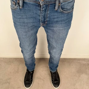 Blå jeans från Jack & Jones - Snygga blå jeans från Jack & Jones med klassisk femficksdesign och bruna sömmar. Modellen har normal passform och raka ben, med en tydlig logopatch bak i midjan. Jeansen är tillverkade i slitstarkt denim och har en stilren look.