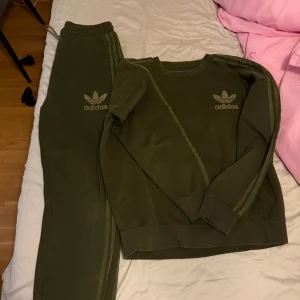 Olivgrön Adidas sweatshirt M Set - Säljer en olivgrön sweatshirt från Adidas Originals i storlek M. Tröjan har klassiska tre ränder längs ärmarna och Adidas-logga på bröstet. Rund hals och långa ärmar, tillverkad i mjuk bomullsmix. Perfekt för chill eller träning.