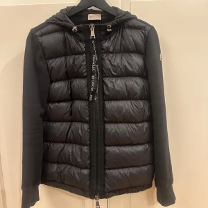 Svart pufferjacka från Moncler- Intressekol - Svart cardigan  från Moncler med huva och långa ärmar. Jackan har quiltad framsida i glansig polyester och släta ärmar med Moncler-logga på vänster arm.  Passar någon som är 165/175 , jag säljer den för att den är för stor för mig och jag är 150 cm. Kom med prisförslag. Endast intresse koll . Storlek 1/S