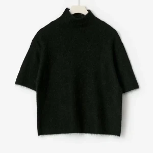 Svart stickad polotröja med kort ärm - Svart stickad polotröja med korta ärmar och hög krage. Tröjan har en loose passform och är tillverkad i ett mjukt stickat material som ger en skön känsla. Perfekt för dig som gillar minimalistisk stil och vill ha något enkelt men snyggt. Bara använd någon enstaka gång i väldigt fint skick! 💕