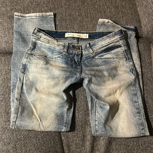 Lågmidjade jeans - Snygga blå lågmidjade jeans från 72D med coolt tvättad och sliten look. Modellen är regular fit med knapp och dragkedja fram. Jeansen har ljusa partier och kontrastsömmar som ger en trendig vibe. Midjan är W26 och passar mig som är typ 165