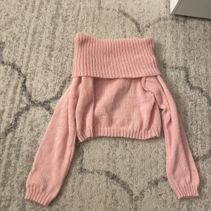 Ljusrosa croppad stickad tröja - Superfin ljusrosa stickad tröja som kan bäras offshoulder. Croppad modell med långa ärmar och ribbade muddar. Perfekt för dig som gillar trendiga och mysiga plagg med lite extra attityd.