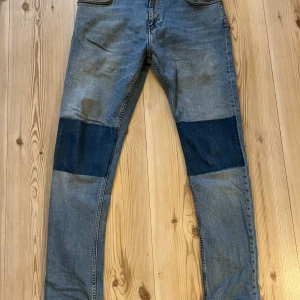 Blå jeans med mörka lappar från Baxter strl.32/32 - Snygga ljusblå jeans från Baxter Denim med mörkblå lappar över knäna som ger en cool kontrast. Klassisk femficksmodell och broderad logga i midjan. Jeansen har en rak passform och är tillverkade i slitstarkt denimtyg.