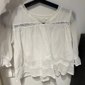 Vit blus med spets från Gina Tricot - Säljer en söt vit blus från Gina Tricot i storlek 134/140. Blusen har långa ärmar med lätt puff och elastiska muddar, samt fina spetsdetaljer vid halsringning och över bröstet. Tillverkad i mjuk bomull med luftig och flowy passform.