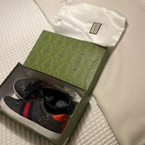 Gucci ace  - Snygga Gucci sneakers med svart bas, röda och blå ränder på sidan och tigermotiv. Skorna är lite skadade på olika ställen men fungerar fortfarande perfekt till användning. Kan gå med på att gå ner vi (snabbt) köp.