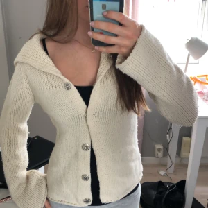 Vit stickad kofta med stora knappar - Mysig vit stickad kofta med stora silvriga knappar framtill och breda ärmar. Koftan har en bred krage och är perfekt för lager-på-lager. Passar till många olika stilar och är superbekväm.