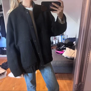 Svart oversized bomberjacka i ull - Svart bomberjacka med oversized passform och raka axlar. Jackan har stora fickor framtill, knappar längs hela framsidan och är tillverkad i ett tjockt ullmaterial. Jackan är i nytt skick men köpt på vinted (inte mina bilder) 
