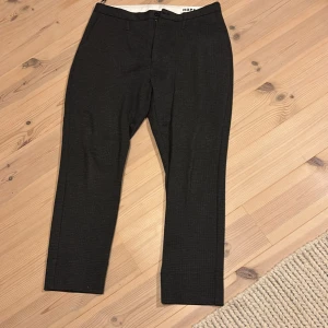 Mörkgrå kostymbyxor från HOPE - Snygga mörkgrå kostymbyxor från HOPE med diskret rutmönster. Klassisk rak passform, midwaist och bälteshällor. Byxorna har fickor både fram och bak, och är tillverkade i ett mjukt material som känns lyxigt. Perfekt för dig som gillar stilrena och moderna plagg. Law trouser