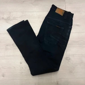 Svarta jeans från Nudie Jeans - Snygga svarta jeans från Nudie Jeans med klassisk femficksdesign och läderpatch bak i midjan. Jeansen har raka ben och är tillverkade i ett mjukt denimtyg som sitter skönt hela dagen.