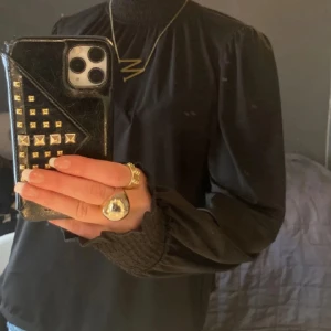 Svart blus med hög krage från Lindex - Säljer en svart blus från Lindex i storlek S. Blusen har en snygg hög krage och långa puffärmar med smock vid ärmslutet. Materialet är mjukt och lätt, perfekt för att ge en cool och stilren vibe. Passformen är normal och blusen är enkel att matcha med dina favoritjeans.