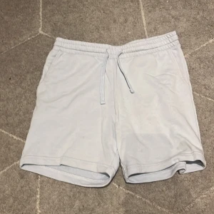 Ljusgrå shorts från H&M med snörning - Säljer ett par ljusgrå shorts från H&M i regular fit. De har elastisk midja med snörning, sidofickor och en bakficka. Perfekta för varma dagar och chill häng. Materialet känns mjukt och bekvämt.