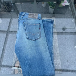 Replay Anbass Jeans – Slim Fit – Strl 30 - Snygga original Replay Anbass i storlek 30. Ljus denim med naturligt slitage. Slim passform med stretch – sitter tajt men bekvämt. Klassiska Replay-detaljer på fickorna + läderpatch bak.  Skick: Fint använt skick. Inga hål, bara normal tvättad look. Material: Bomull med elastan (stretch – sitter riktigt bra).  Perfekta som vardagsjeans eller till en clean outfit. 