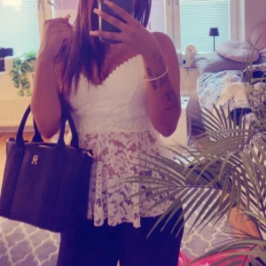 Vit spetsig linnetopp med volang - Superfin vit linnetopp med spets och volang nertill. Toppen har smala axelband och v-ringad urringning med dekorativ kant. Spetsen är blommig och ger en romantisk vibe, perfekt till ljusa jeans eller kjol. Sval och luftig för varma dagar.