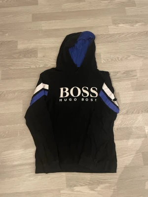 Svart hoodie från Hugo Boss med blå detaljer - Hoodien har används många gånger, hoodien är ganska tunn, säljer den pga den passar inte mig, passar de som har xs. Priset kan diskuteras 