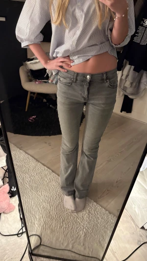 Grå bootcut jeans låg midja - Säljer ett par grå jeans med låg midja och bootcut-ben. Jeansen har klassisk femficksdesign och är i ett mjukt denimtyg. Snygg passform som sitter tajt upptill och släpper ut vid anklarna. Perfekta till sneakers eller boots.