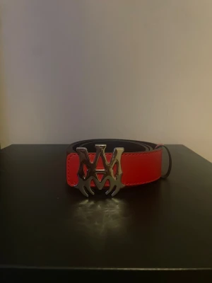 Rött skärp med stor metallspänne - Snyggt rött bälte med bred rem och ett stort, unikt metallspänne i silverfärg. Bältet har en stilren design med markerade sömmar och passar perfekt för att ge outfiten en edgy touch.