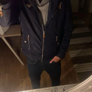 Mörkblå morris jacka  - Snygg mörkblå vindjacka från Morris med silvriga dragkedjor och detaljer i brunt. Jackan har två fickor framtill, ribbad nederkant och ett broderat märke på bröstet. Perfekt för dig som vill ha en stilren och sportig look. Nypris ca 2800, pris kan diskuteras 