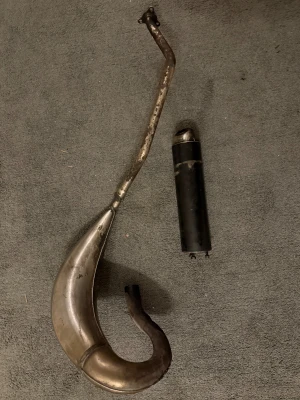 Technigas Avgassystem - Komplett avgassystem från technigas, med expansionskammare och ljuddämpare. Passar cross/moped. Synligt slitage och repor, men inga större bucklor. Perfekt för dig som vill uppgradera prestandan. Ljuddämparen är svart och har technigas-logga.