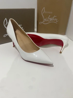 Vita pumps från Christian Louboutin - Säljer ett par klassiska vita pumps från Christian Louboutin med den ikoniska röda sulan. Skorna har spetsig tå, hög klack och är tillverkade i glansigt skinn. Perfekta för dig som vill sticka ut med en elegant och tidlös look.