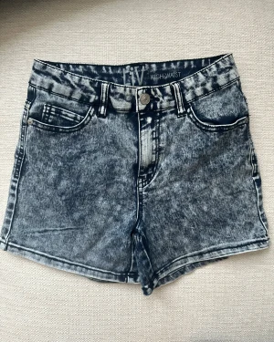 Acid wash highwaist shorts från dELiA*s - Snygga acid wash denimshorts från dELiA*s med hög midja och klassisk femficksdesign. Färgen är en mörkgrå och svart tvättad look med tydliga kontraster. 