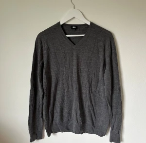 Grå v-ringad tröja från Uniqlo - Snygg grå v-ringad tröja från Uniqlo i ren ull. Klassisk modell med lång ärm och ribbade muddar vid ärmslut och nederkant. Perfekt för dig som gillar stilrena och enkla plagg med skön passform. Storlek L. 4Ä2
