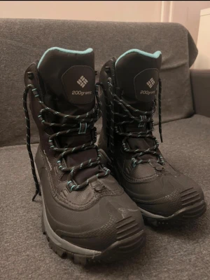 Svarta vinterkängor Columbia strl 39 - Säljer ett par svarta vinterkängor från Columbia med turkosfärgad insida och detaljer på snörningen. Grov sula för extra grepp och slitstarkt syntetmaterial. Perfekta för kalla dagar och utomhusaktiviteter. Modell WMN'S BL5980-010.