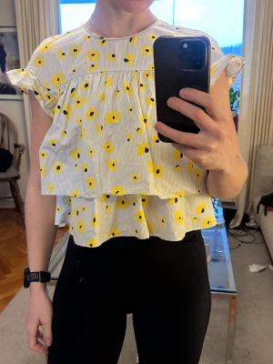 Blommig blus från Zara  - Supersöt blus från Zara med volangärmar och blommigt mönster i gult och svart på vit bakgrund med tunna grå ränder. Blusen har knappar i ryggen, en har tyvärr lossnat men går givetvis att sy på ny.