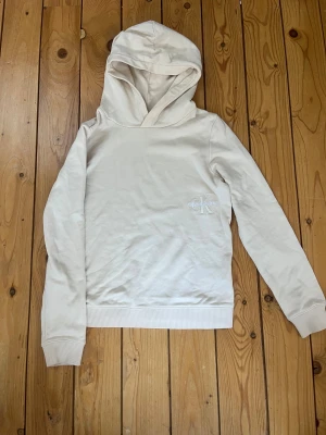 Beige hoodie från Calvin Klein - Snygg vit/beige hoodie från Calvin Klein Jeans med broderad logga på bröstet. Tillverkad i mjuk bomull som är skön att ha på sig. Använd ändats en gång så i jättebra skick.
