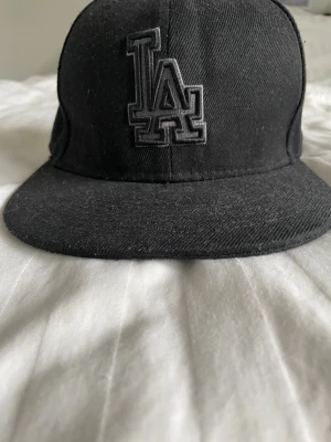 Svart MLB  LA Dodgers keps - Säljer en svart LA Dodgers keps från New Era med broderad LA-logga framtill och MLB-logga bak. Klassisk modell med rak skärm och sex paneler. Kepsen är i bomull och passar dig som gillar stilren streetwear. Kepsen är i fint skick och passar perfekt. Dessa kepsar är otroligt populära och säljer slut snabbt!