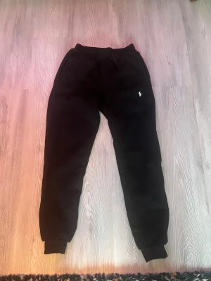  mjukisbyxor från Polo Ralph Lauren - Svarta mjukisbyxor från Polo Ralph Lauren med klassisk broderad logga på benet. Byxorna har resår och snörning i midjan samt muddar vid bensluten. Perfekta för en chill och stilren look.