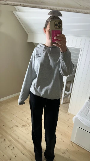 Grå hoodie från Gina Tricot med tryck - Grå hoodie från Gina Tricot med svart texttryck 'JE M'EN AMOUR' och en stjärna på ryggen. Tröjan har huva, snörning och långa ärmar. Mjuk insida och avslappnad passform, perfekt för chill dagar. Små fläckar på axeln (se bild 4) men inget man tänker på💕