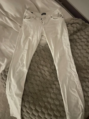 Vita jeans från The Black Label Collection - Snygga vita jeans från The Black Label Collection med silverfärgade nitar vid fickorna och klassisk femficksdesign. Byxorna har en rak passform och är tillverkade i ett mjukt bomullsmaterial. Perfekt för dig som gillar stilrena och fräscha looks. Byxorna är också köpta från året 2000s så dom är väldigt low waist, skulle vara assnyggt med ett par höga boots nu till hösten/vintern, Pris kan diskuteras 