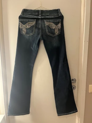 Mörka bootcut jeans Gina Tricot 164 - Snygga mörkblå bootcut jeans från Gina Tricot i storlek 164. Jeansen har dekorativa bakfickor med broderade detaljer och bling, samt tydliga kontrastsömmar. Klassisk femficksmodell i stretchigt denimtyg.