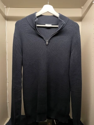 Mörkblå stickad half zip från John Henric - Snygg mörkblå stickad tröja från John Henric med ribbad struktur och half zip-dragkedja vid halsen. Tröjan har lång ärm och en lite högre krage som ger en chill och stilren vibe. Perfekt för dig som gillar klassisk men modern look.