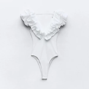 Vit volangbody - Säljer en stilren vit ribbad body med volangdetaljer vid axlarna. Den har en djup v-ringning. Passar bra till både jeans och kjol. Köpt här på plock (förra säljarens bilder). 