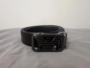 Svart skärp från Giorgio Armani - Snyggt svart bälte från Giorgio Armani i skinn med en bred, rektangulär spänne med logotypen i metall. Bältet är 3 cm brett och har stilrena detaljer längs kanten. Perfekt för dig som vill ha en exklusiv och modern look.
